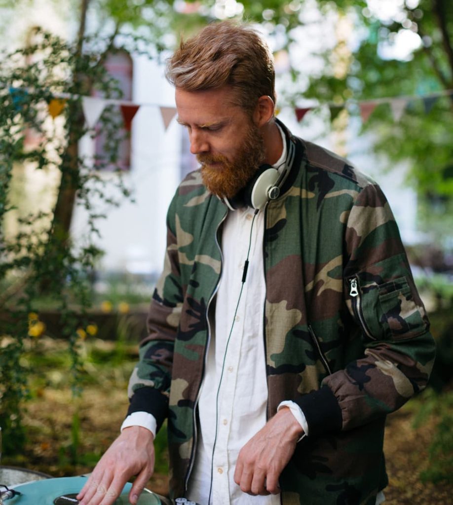 Micke Sonnenberg i kamouflagejacka, vit skjorta och hörlurar runt halsen då han jobbar som DJ