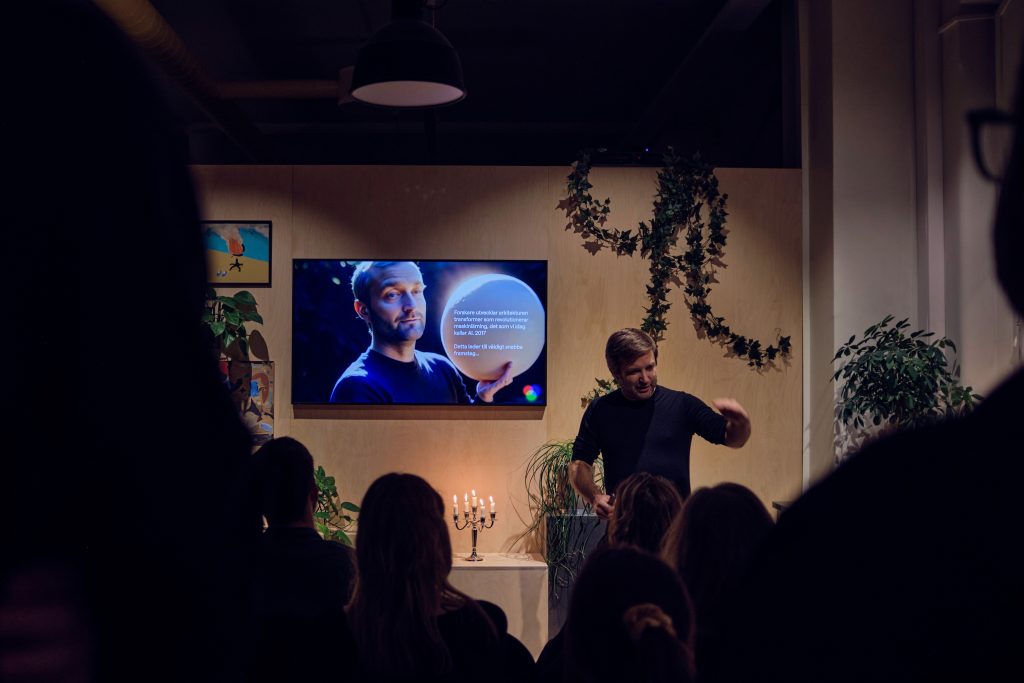 En man håller en föreläsning för en publik framför en skärm.